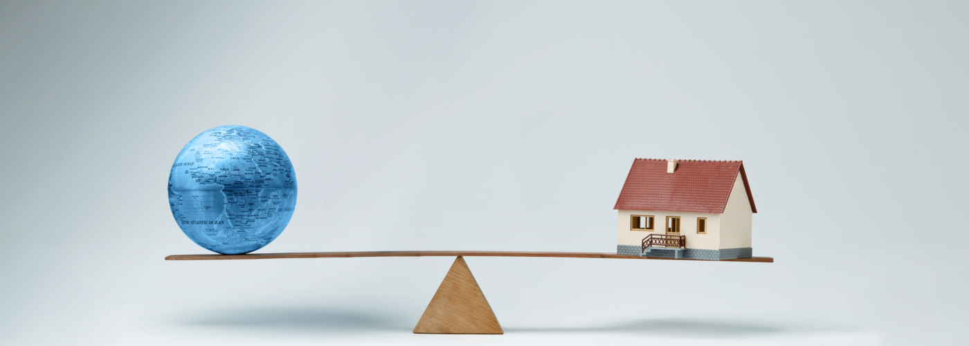 World globe and model house balancing on a seesaw
